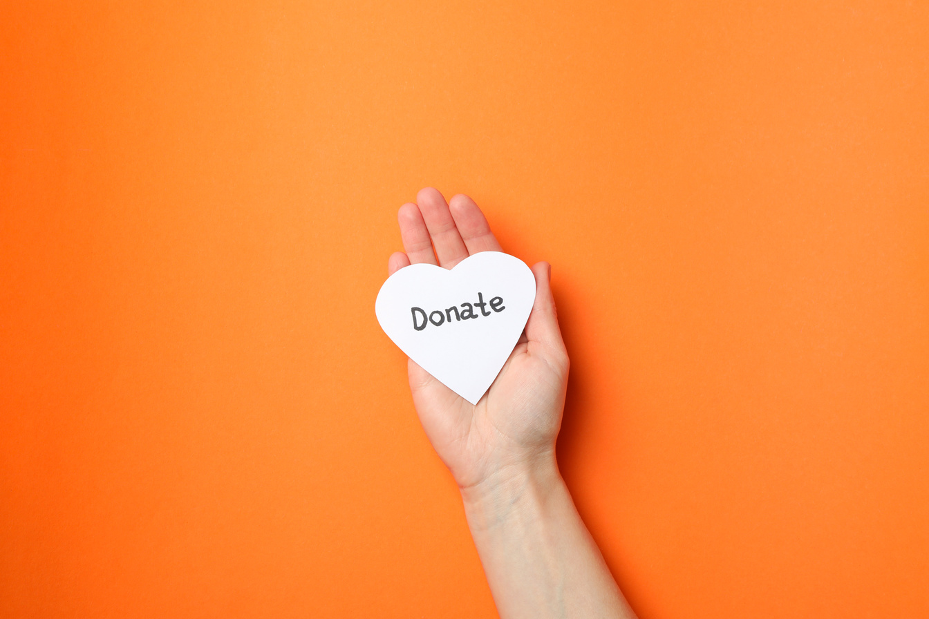 Female Hand Holds Heart with Inscription Donate on Orange Backgr